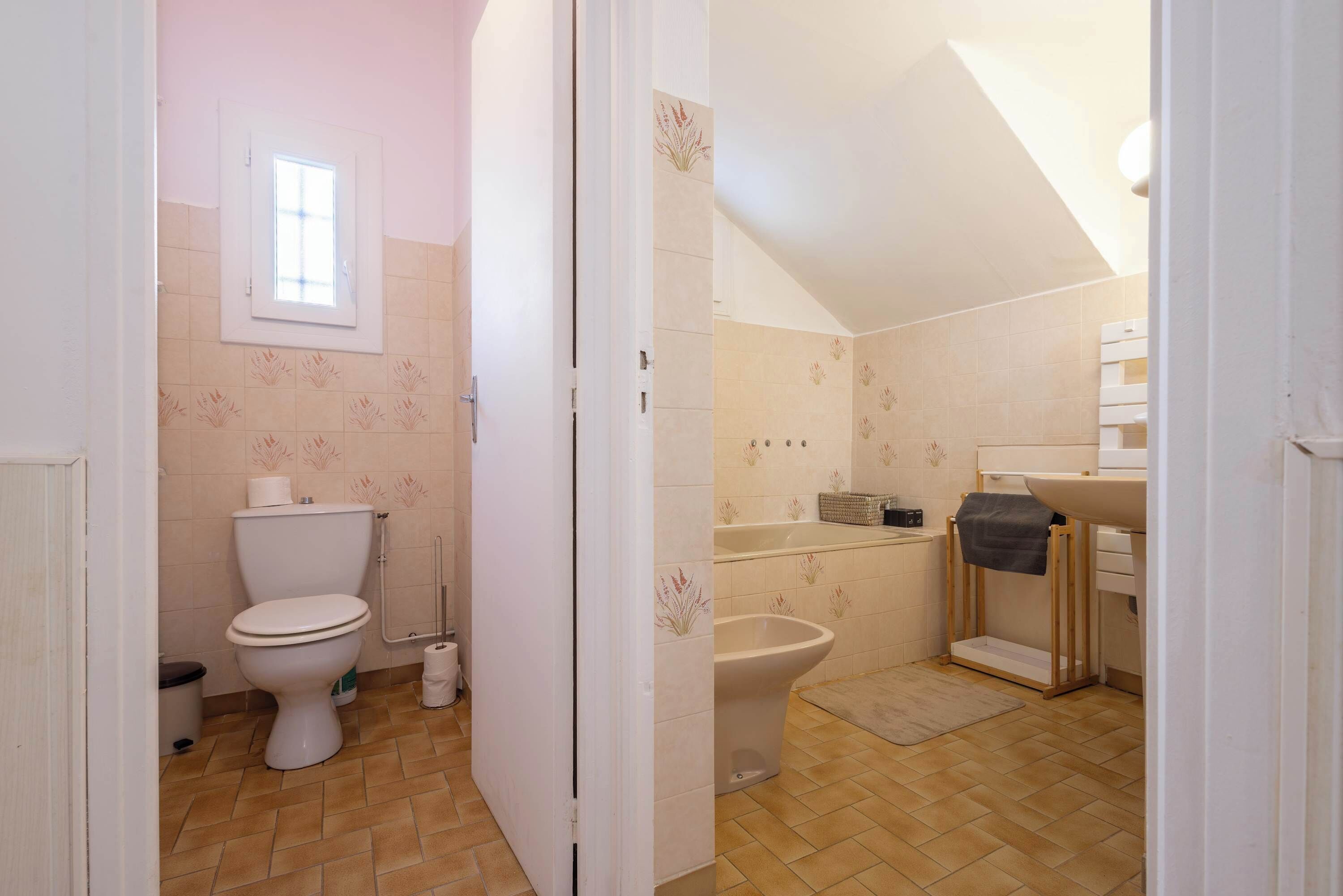 Ein Badezimmer mit Toilette, Bidet, Waschbecken und einem Fenster.