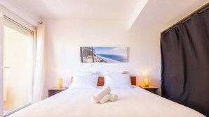 Una camera d'hotel con un letto, un quadro raffigurante una spiaggia, due abat-jour e una finestra con tende.