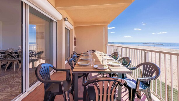Un balcone con tavolo apparecchiato per mangiare, sedie e vista sulla spiaggia.
