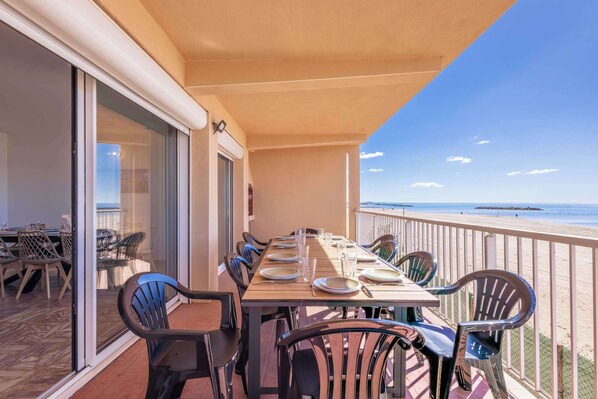 Un balcon avec une table dressée pour le dîner, des chaises et une vue sur la plage.