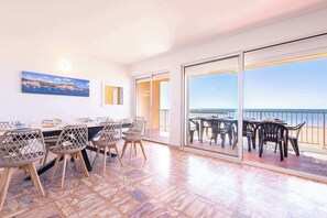 Une pièce spacieuse avec une grande table et des chaises, un tableau au mur et un balcon avec vue sur la mer.