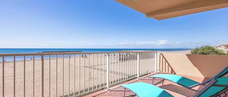 A balcony with a view of the beach, metal railings, and two green lounge chairs.