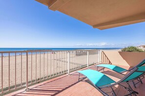 Un balcon donnant sur la plage, avec des rampes en métal et deux fauteuils de jardin verts.