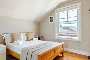 Ein Schlafzimmer mit einem hölzernen Bett, einem Nachttisch, einem Fenster mit Blick und einem kleinen Bild an der Wand.