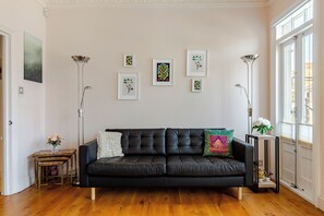 Ein Wohnzimmer mit einem schwarzen Ledersofa, einem kleinen Tisch mit Blumen und gerahmten Pflanzenbildern an der Wand.