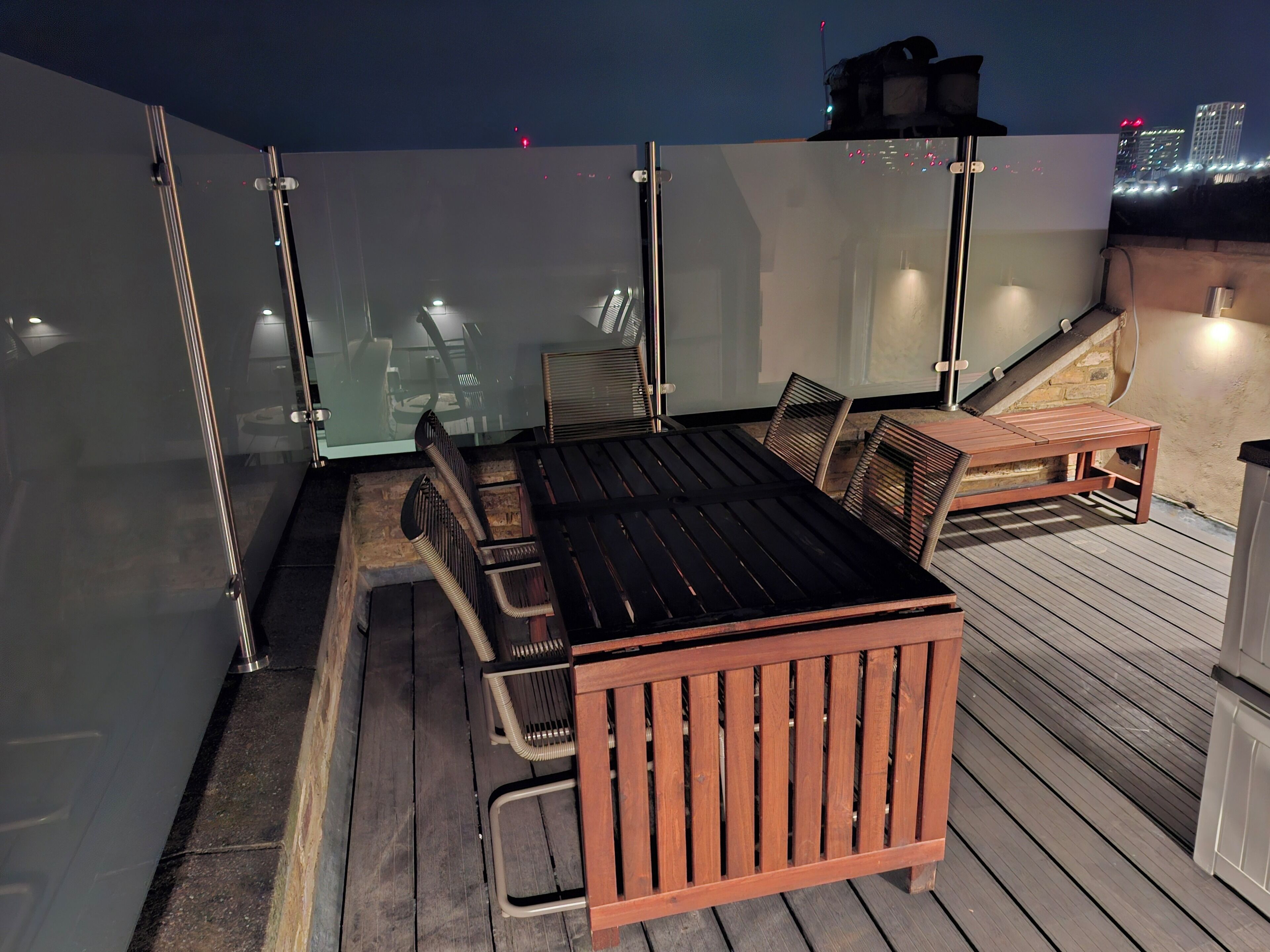 Une terrasse sur le toit, avec une table et des chaises en bois, des portes vitrées et une vue sur le panorama urbain.