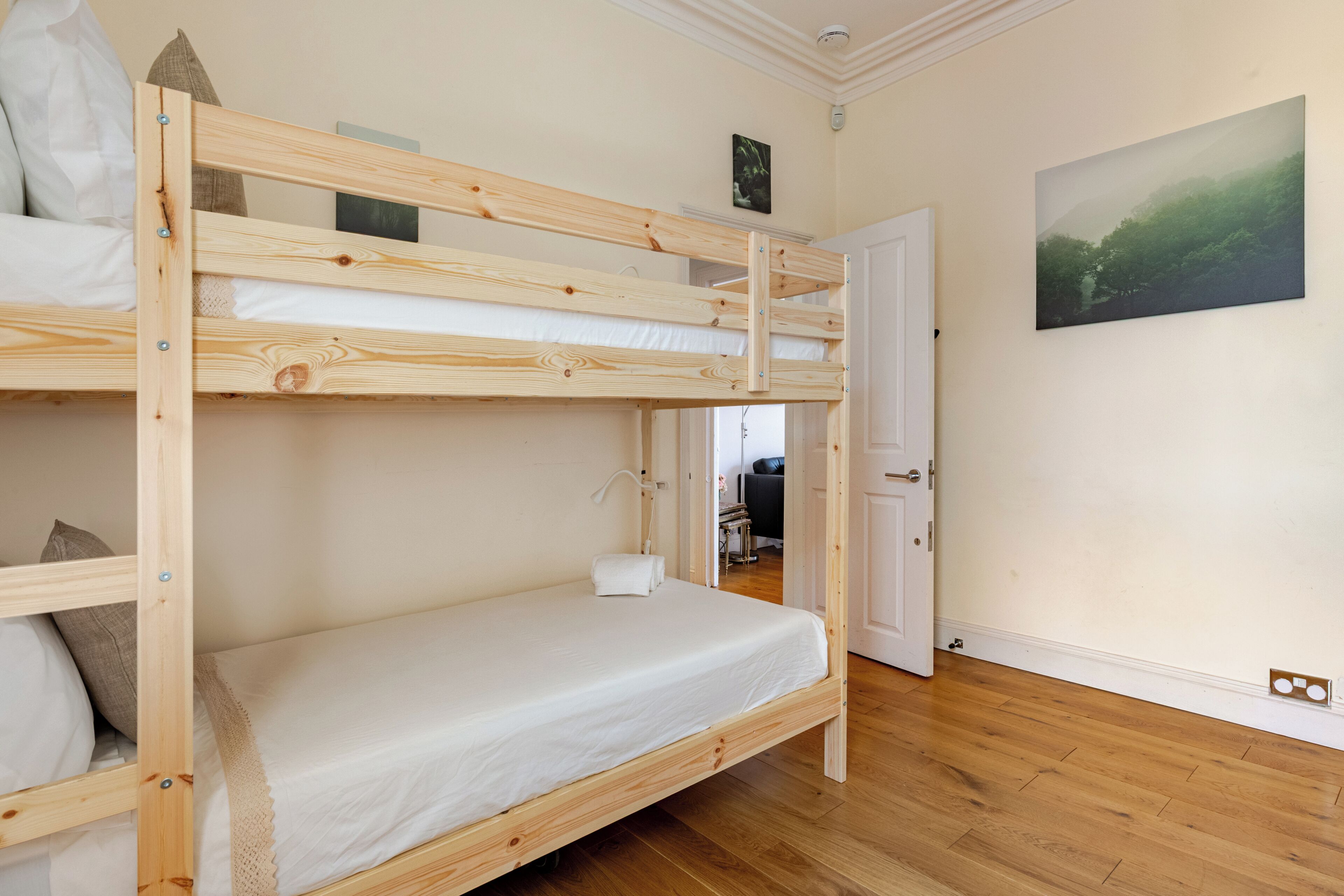 A bunk bed room with a wooden floor, a white door, and a framed picture on the wall.