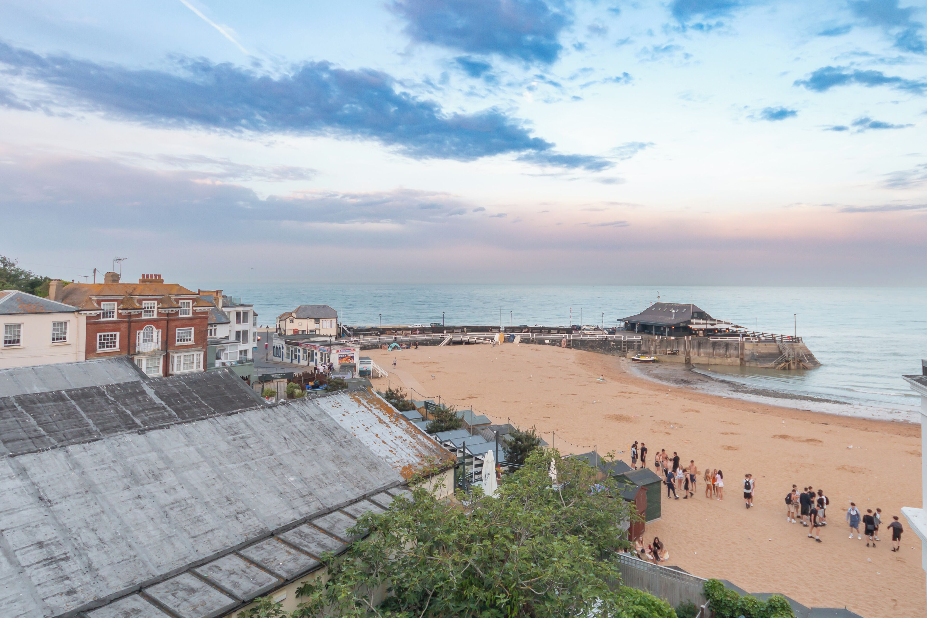 Una playa con un muelle, edificios al fondo y un cielo despejado.