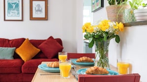 A dining table with breakfast items, a red chair, and a red sofa in the background. - Enjoy a cosy 2-bedroom cottage-style stay in Broadstairs, just around 2 minutes from the beach and close to Viking Bay. Sleeps up to 4 guests with a double bedroom, bunk room, good Wi-Fi, comfortable living space, kitchen/dining area, washing machine (Kent)