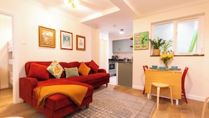 A living room with a red sofa, a dining area with a wooden table and chairs, and a kitchen in the background. - Enjoy a cosy 2-bedroom cottage-style stay in Broadstairs, just around 2 minutes from the beach and close to Viking Bay. Sleeps up to 4 guests with a double bedroom, bunk room, good Wi-Fi, comfortable living space, kitchen/dining area, washing machine (Kent)