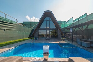 En swimmingpool med et glasafskærmning, omgivet af liggestole og et overdækket område.