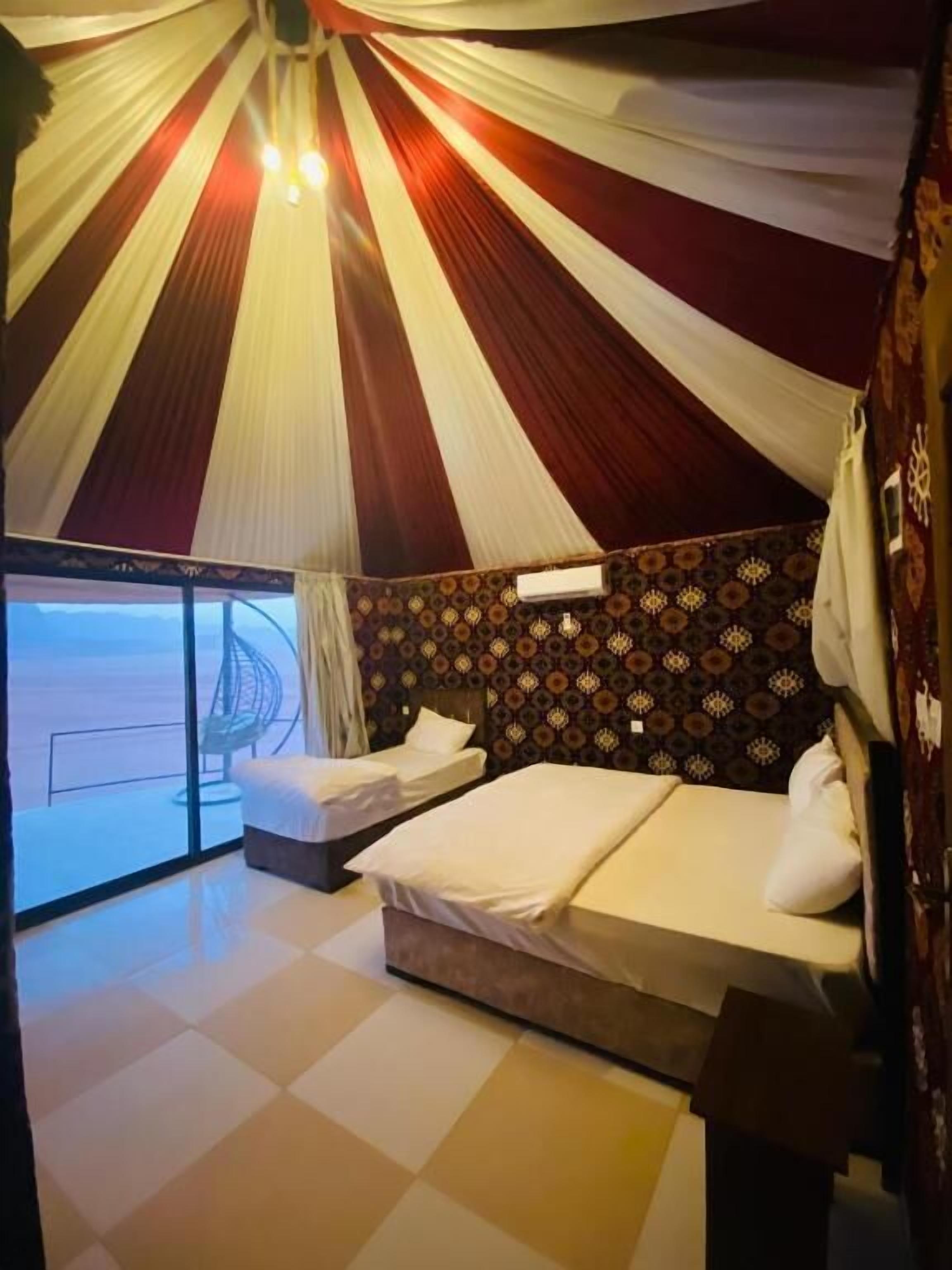 A room with two beds, a patterned wall, a large window, and a curtain.