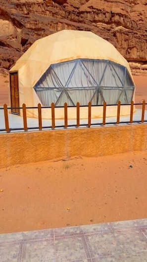 A dome-shaped tent-like structure with a door, surrounded by a wooden fence, set against a rocky background.
