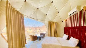 Um quarto tipo tenda com cama, cortinas, uma cadeira e vista para o deserto.