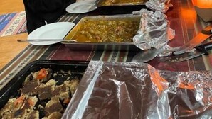 Disposição de buffet com diversos pratos, uma vela e uma parede listrada ao fundo.