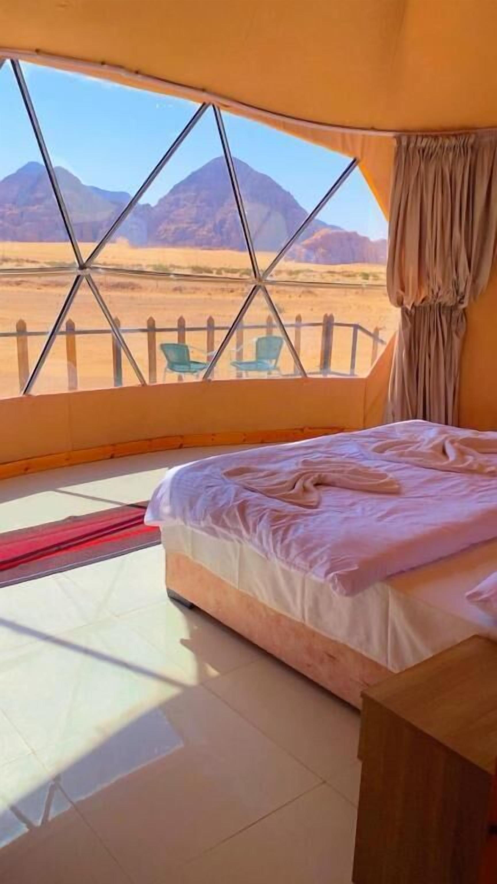 Ein Zimmer mit einem Bett, einem Fenster mit Bergblick, einem Vorhang und einem Nachttisch aus Holz.