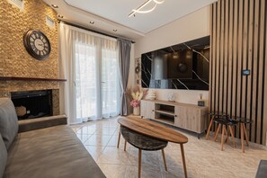 Ein modernes Wohnzimmer mit Kamin, großem Flachbildfernseher, Couchtisch aus Holz und einer Couch.