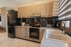 Eine moderne Küche mit Holzschränken, einem schwarzen Kühlschrank, einer Mikrowelle, einem Toaster und einem Spülbecken.