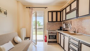 Eine Küche mit Herd, Backofen und Spüle, ein Essbereich mit Tisch und Stühlen sowie eine Glastür zu einem Balkon.