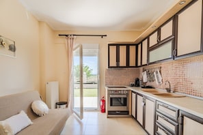 Eine Küche mit Herd, Backofen und Spüle, ein Essbereich mit Tisch und Stühlen sowie eine Glastür zu einem Balkon.