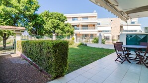 Eine moderne Außenpatio mit Tisch und Stühlen, einer ordentlich geschnittenen Hecke und Blick auf ein mehrgeschossiges Gebäude im Hintergrund.