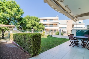 Eine moderne Außenpatio mit Tisch und Stühlen, einer ordentlich geschnittenen Hecke und Blick auf ein mehrgeschossiges Gebäude im Hintergrund.