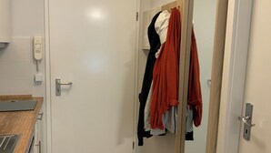 Une pièce avec une porte blanche, un comptoir en bois, un miroir et un porte-manteau sur lequel sont accrochés divers vêtements.