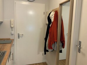 Ein Zimmer mit einer weißen Tür, einer Holzauslage, einem Spiegel und einem Kleiderständer mit verschiedenen Kleidungsstücken.