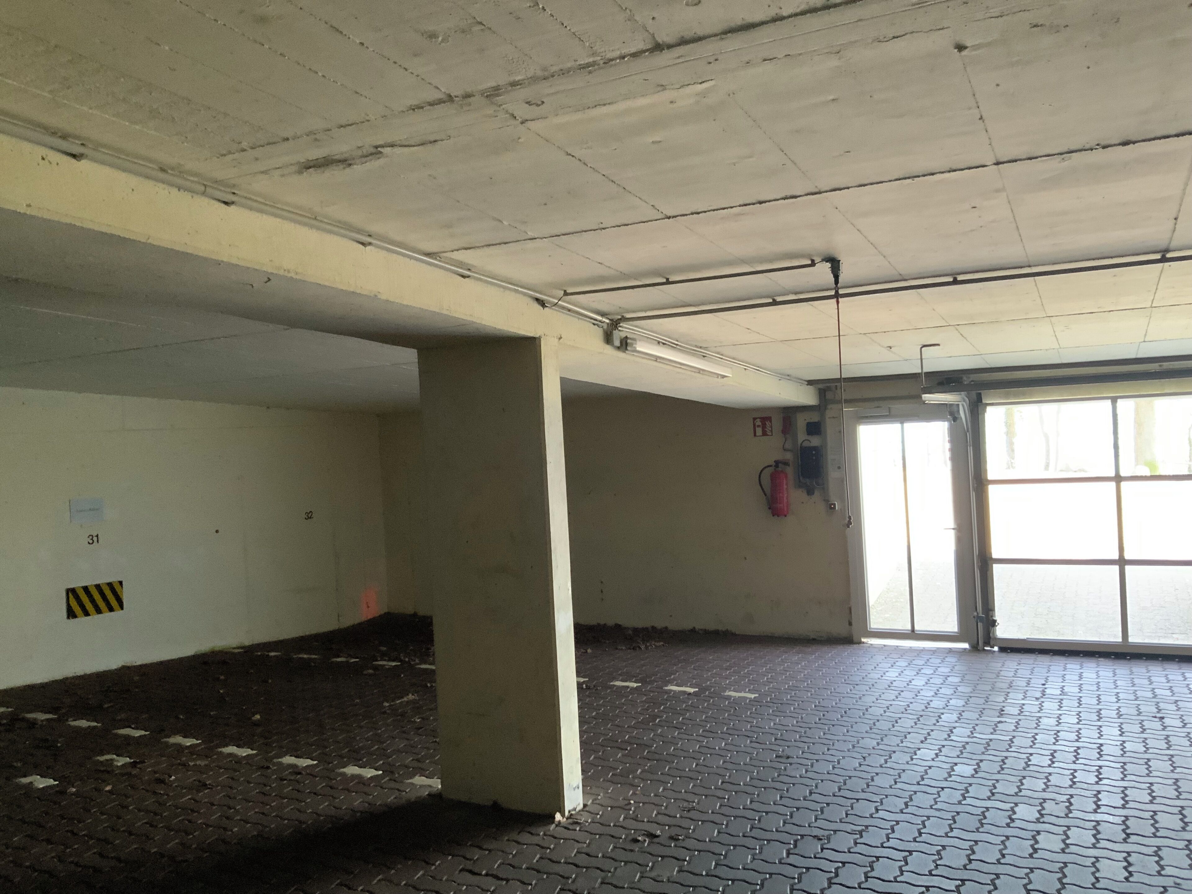 Garagem de estacionamento vazia, com pilares de concreto, um extintor de incêndio e uma porta que dá para o exterior.