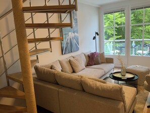 Ein modernes Wohnzimmer mit Treppe, einer Couch, einem Couchtisch und einem Fenster mit Blick auf Grünflächen.