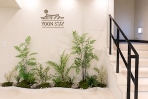 A staircase with a black railing, a wall-mounted sign reading 'YOON STAY,' and a row of green plants with a mossy base. - Yoonstay Haenggung (Suwon)