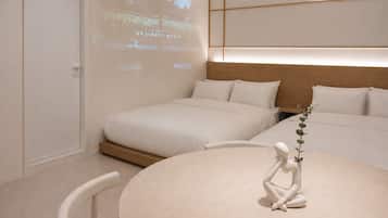 Ein Hotelzimmer mit zwei Betten, einem runden Tisch und einer Projektionsleinwand, die eine Stadtansicht zeigt.