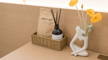 A wicker basket with a brown paper bag labeled 'AMENITY SET' and a white ceramic vase with yellow flowers.