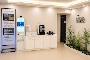 Zona de recepción con un quiosco, una máquina de café y un cartel en la pared.
