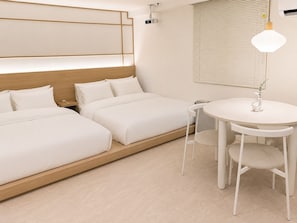 Une chambre d’hôtel avec deux lits, une table ronde avec des chaises, une lampe fixée au mur et un projecteur fixé au plafond.