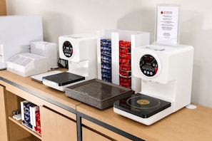A kitchen area with a coffee machine, a rice cooker, and a stack of trays.