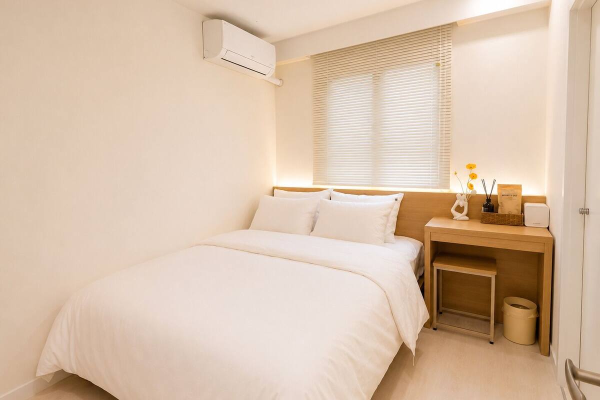 A bedroom with a bed, bedside table, lamp, and an air conditioning unit.