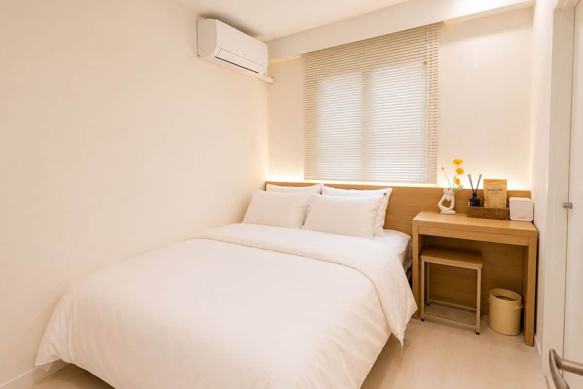A bedroom with a bed, bedside table, lamp, and an air conditioning unit.