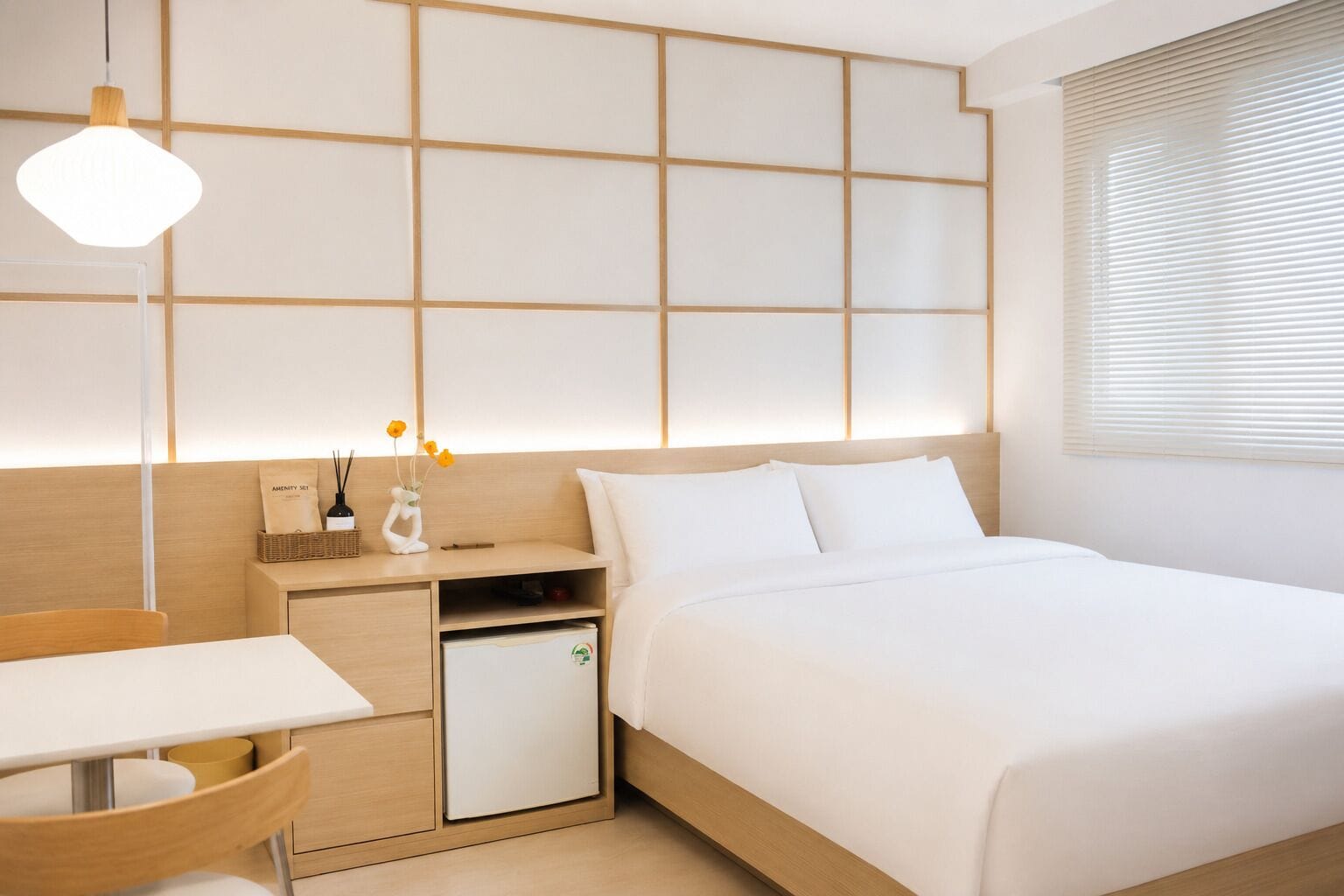A modern hotel room with a bed, bedside table, desk, and a small refrigerator.