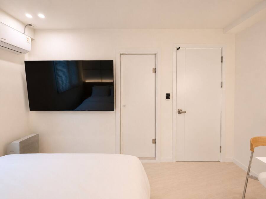 A bedroom with a bed, a TV mounted on the wall, two white doors, and a chair.