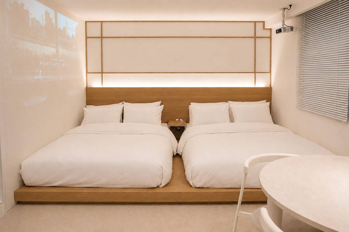 A modern hotel room with two beds, a wooden headboard, a bedside table, and a small round table.