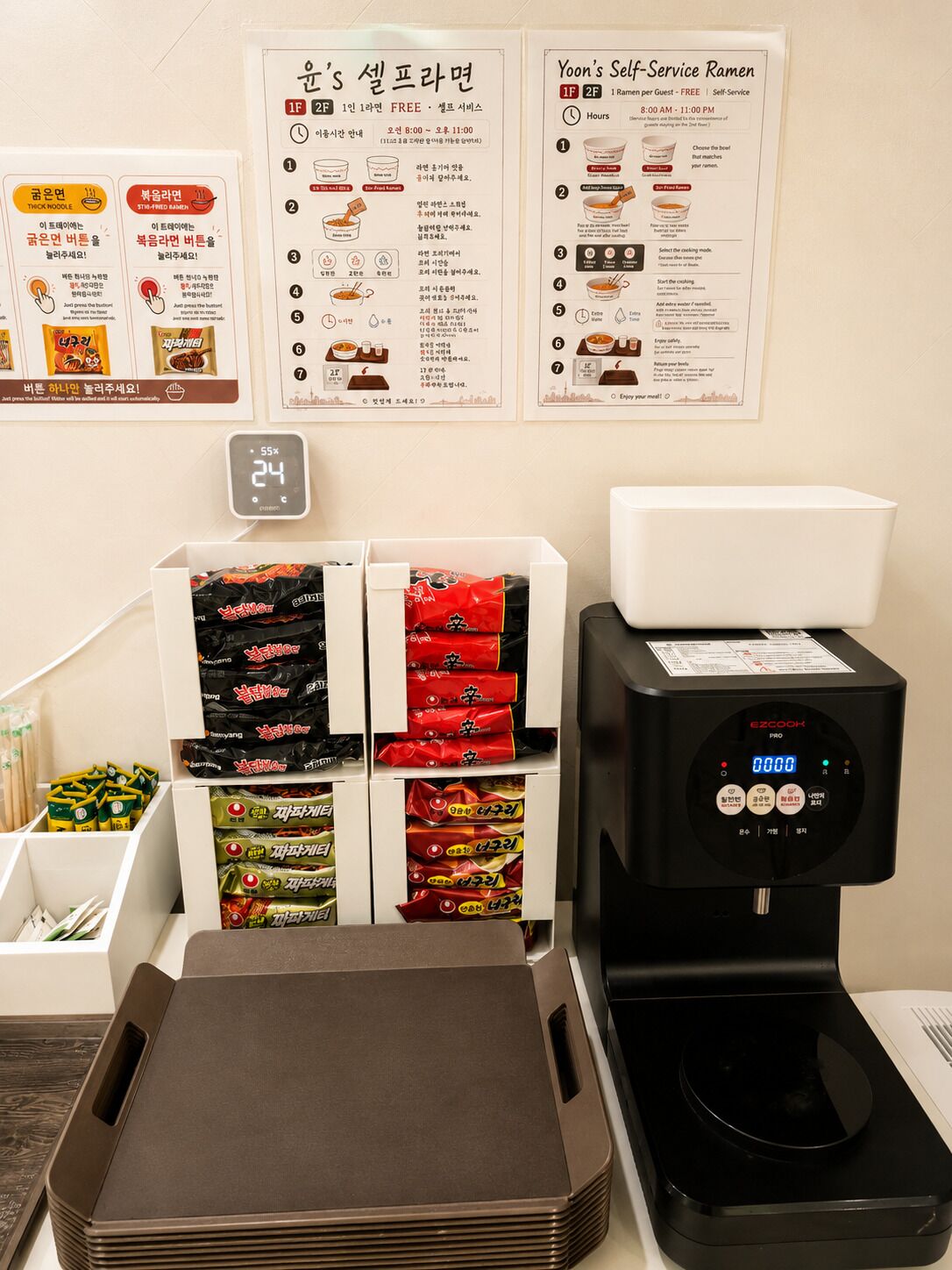 Un puesto de ramen de autoservicio con pantalla digital, dispensadores de condimentos y diversas opciones de ramen envasado.