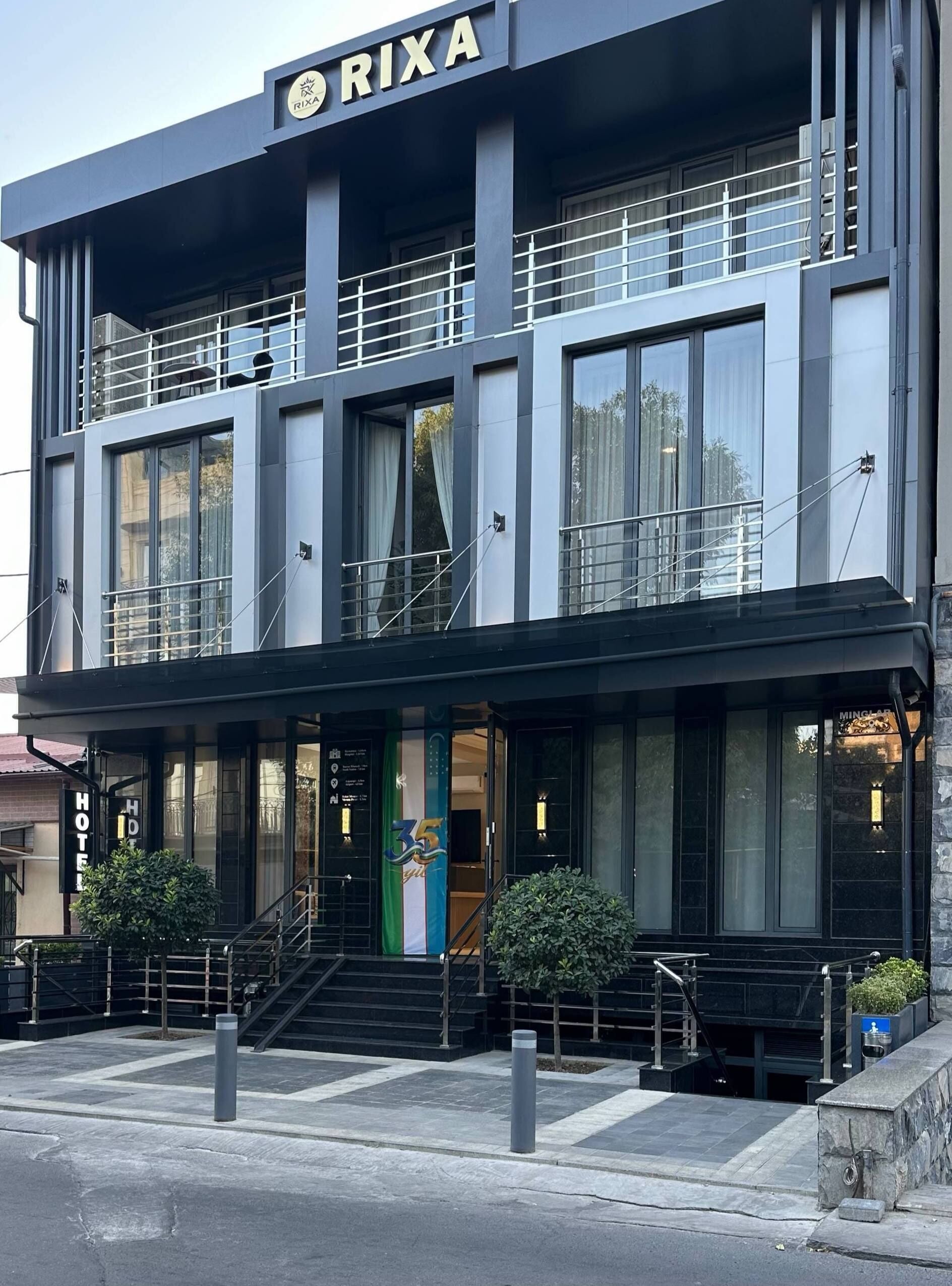 A modern hotel building with a prominent 'RIXA' sign, multiple balconies, and a welcoming entrance with a staircase.