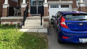 Una casa a due piani con un portico anteriore, un garage e un'auto blu parcheggiata davanti.
