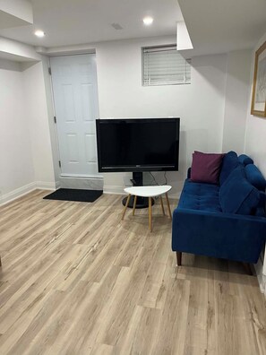Ein Wohnzimmer mit einem Flachbildfernseher, einem blauen Sofa und Holzboden.