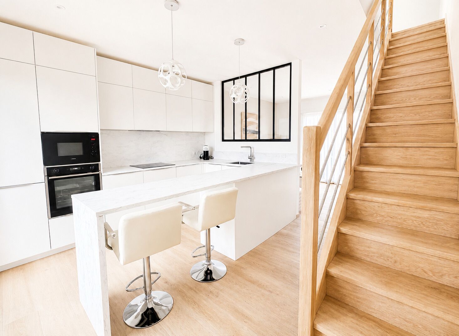 Une cuisine moderne avec des meubles blancs, un escalier en bois et un îlot central doté de tabourets de bar.