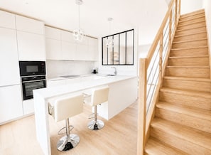 Eine moderne Küche mit weißen Schränken, einer Holztreppe und einer zentralen Kochinsel mit Barhocker.