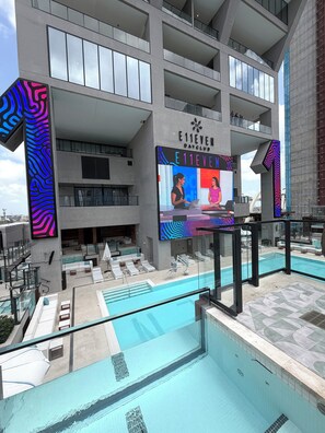 Un hôtel moderne doté d’une piscine sur le toit, d’un grand panneau d’affichage numérique et d’une structure à plusieurs niveaux.