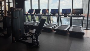 Ein Fitnessstudio mit Laufbändern, Trainingsgeräten und großen Fenstern mit Blick auf die Stadt.