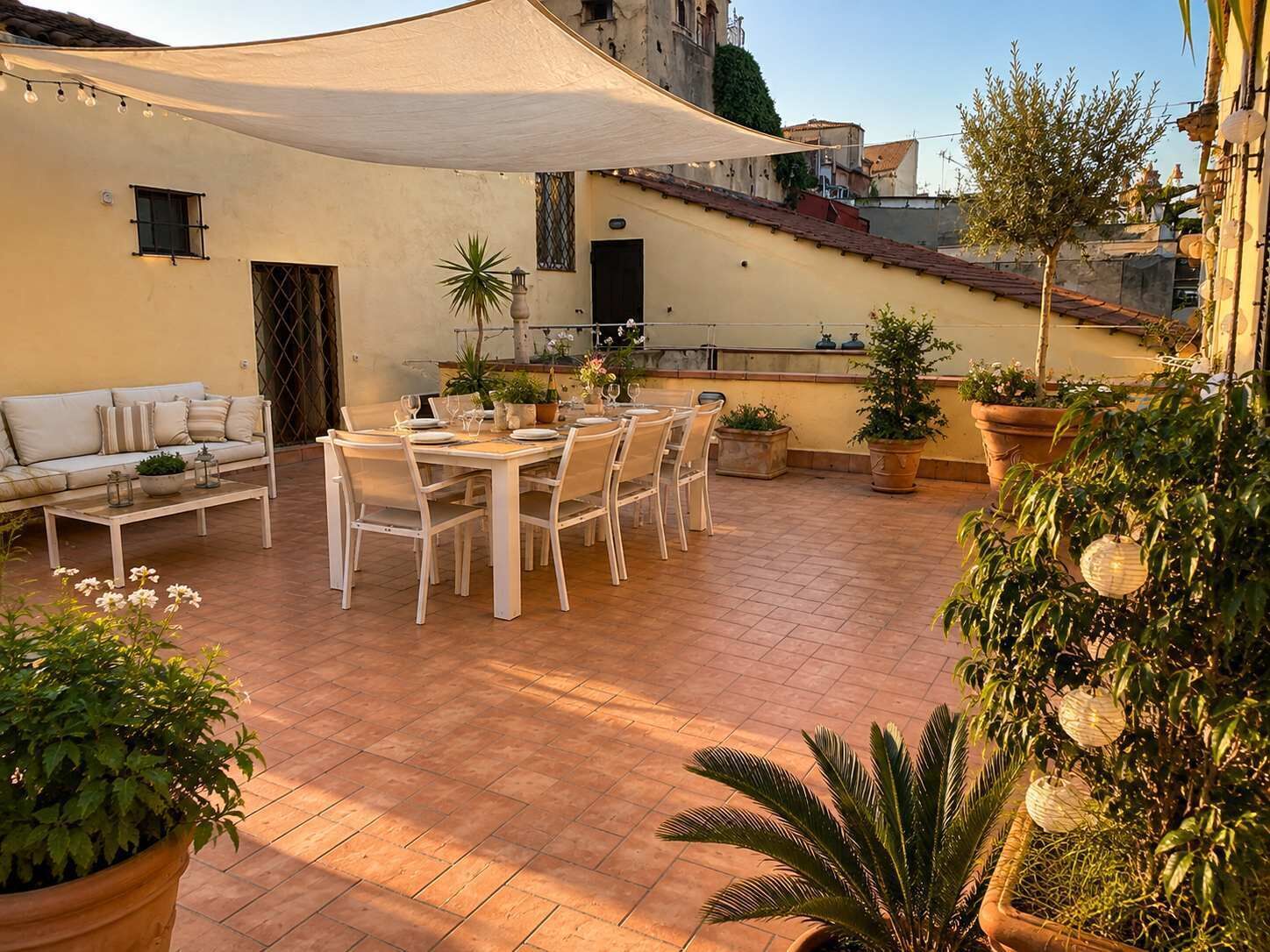 An outdoor patio with a dining table set for six, surrounded by potted plants and a white sofa.